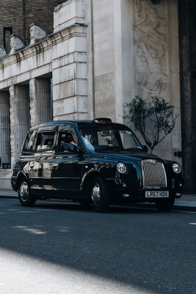 a black taxi cab driving down a street next to a tall building