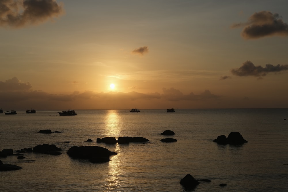 the sun is setting over the ocean with rocks in the foreground