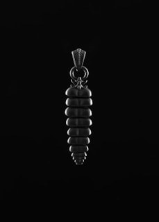 A black and white image of a pendant that resembles a vertical, segmented form with a loop at the top for attachment. The design appears to be symmetrical and textured, suggesting a modern or contemporary artistic style.
