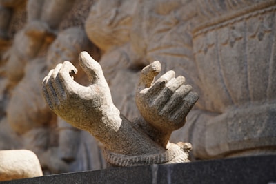 Two intricately carved stone hands are positioned against a textured stone background, with the fingers gracefully curving inward. The details in the carving suggest a significant level of craftsmanship, evoking historical and artistic significance.