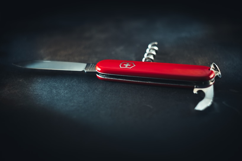 A classic red Swiss Army knife is placed on a dark background, showcasing its multi-functional design with visible tools such as a blade, corkscrew, and bottle opener.