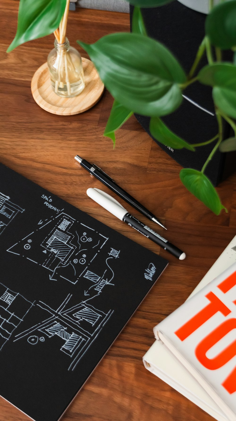 a desk with a notebook, pen and a plant