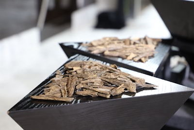 A close-up view of two black, triangular display stands holding piles of light brown wood chips or bark pieces, placed on a reflective surface.