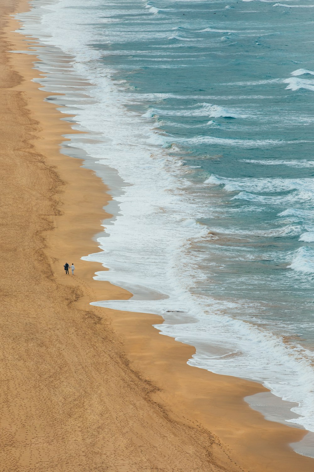 Ein paar Leute spazieren an einem Strand neben dem Meer entlang