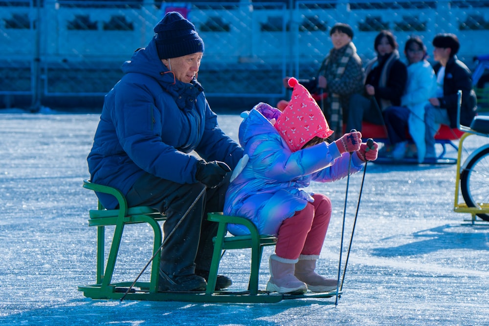 a man sitting on a green bench next to a little girl