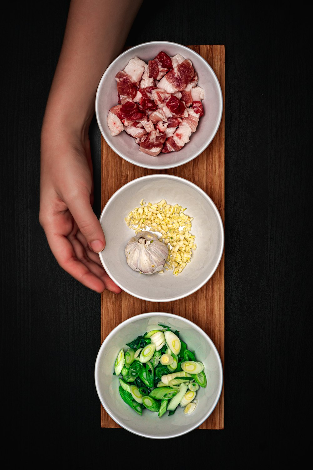 a person holding a knife over three bowls of food