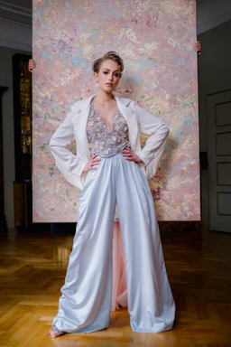 A model wearing a richly embroidered winter party suit, standing against a cozy indoor backdrop.