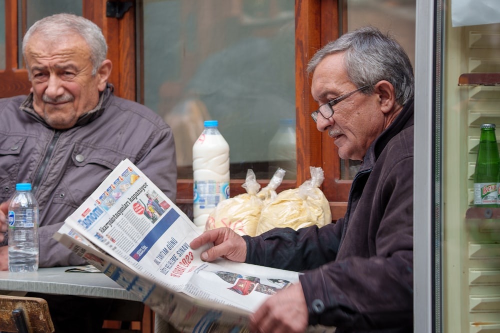 two older men sitting at a table reading a newspaper