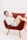 A person is lounging comfortably on a plush, red chair with wooden legs. They are wearing a white shirt and have a relaxed, smiling expression. The background is a plain, light color, enhancing the focus on the person and chair.