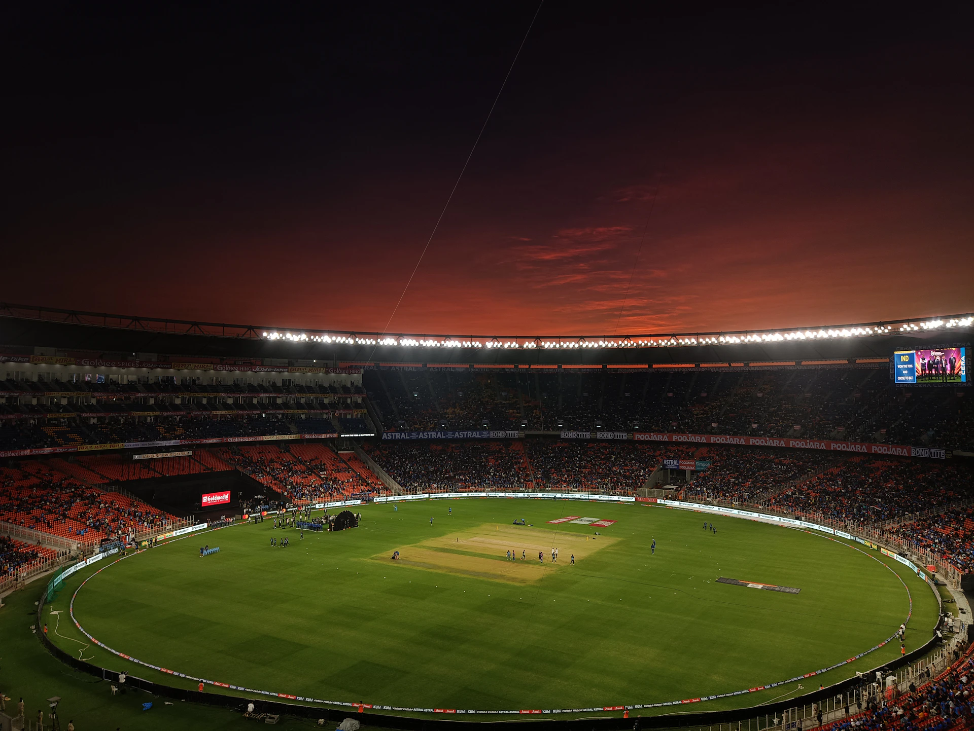 a baseball stadium with a full field and a red sky