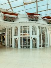 A high-end boutique with an elegant storefront featuring large glass windows and mannequins displaying formal attire. The store's name is displayed prominently above the entrance. The roof has geometric patterns, and there are decorative flower arrangements above.