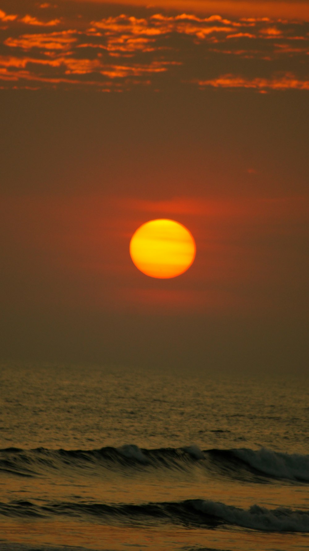 the sun is setting over the ocean on a cloudy day