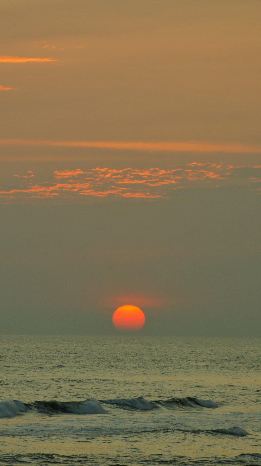 the sun is setting over the ocean on a cloudy day