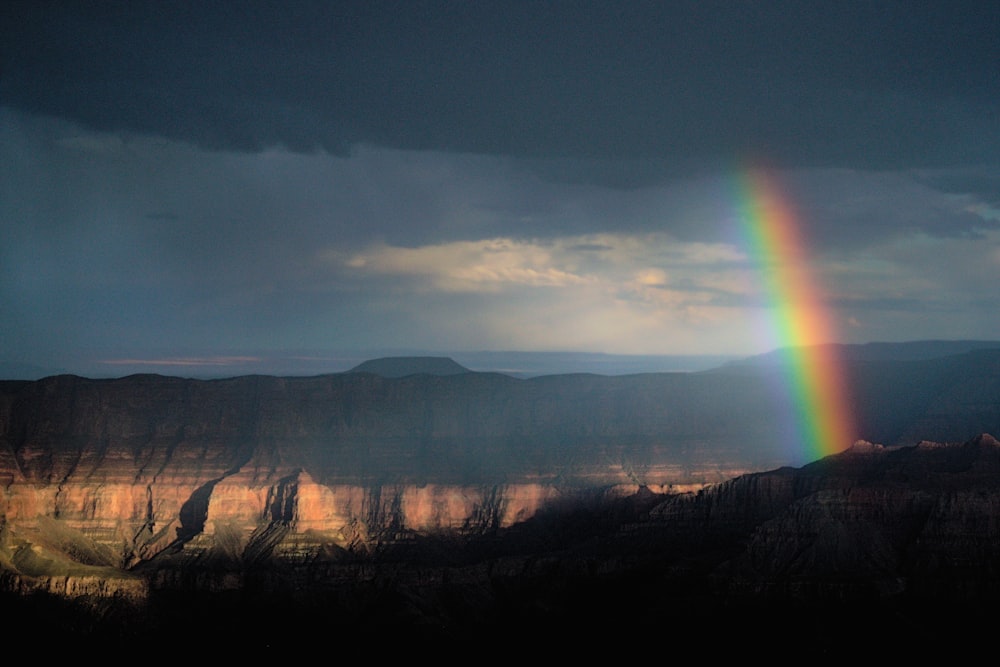 a rainbow shines in the sky over a canyon