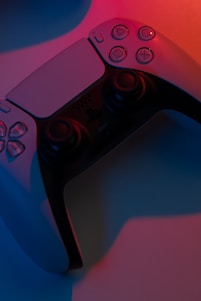 A close-up view of a game controller illuminated by contrasting blue and red lighting, providing a dramatic shadow effect. The controller features button details and analog sticks, reflecting modern gaming design aesthetics.