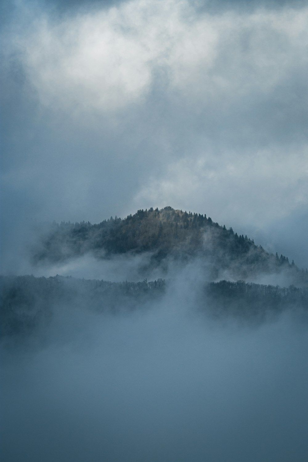 a mountain covered in fog under a cloudy sky