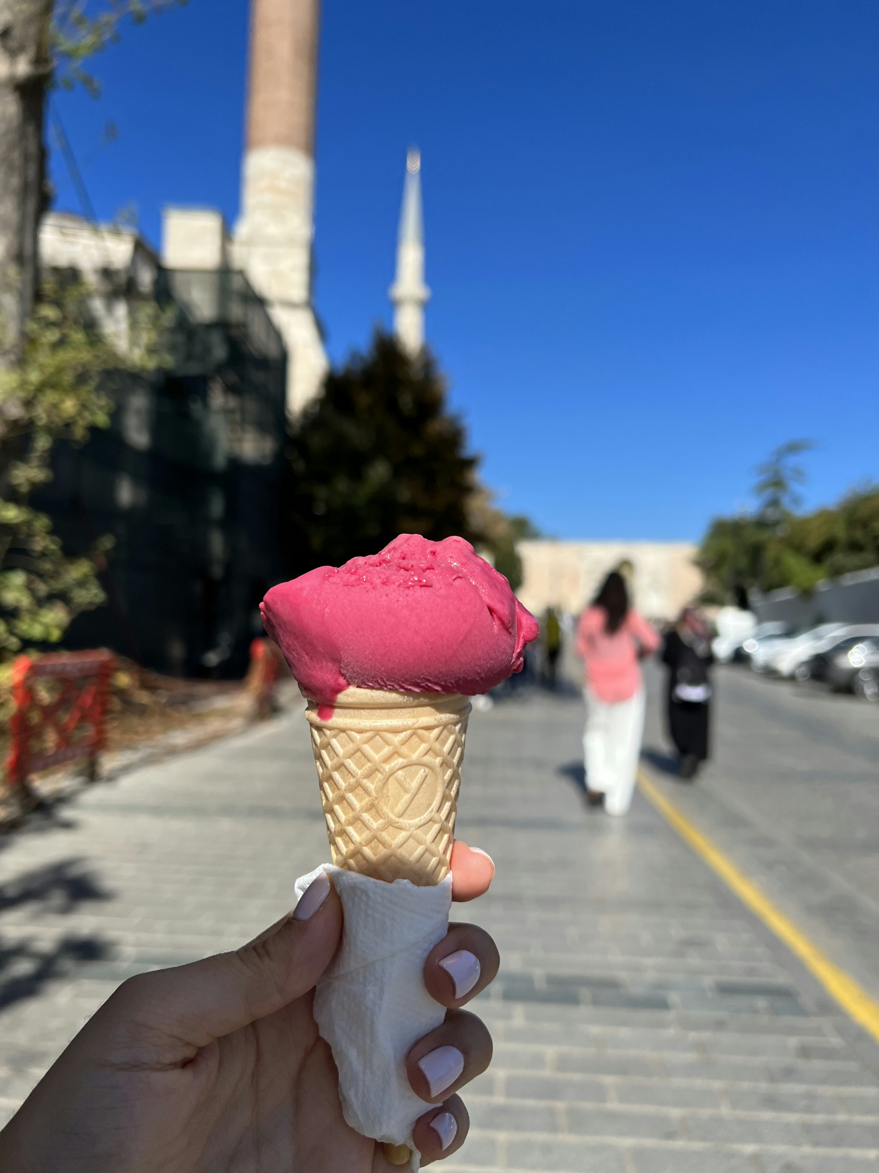 A hand holding an ice cream cone with pink icing photo Free Dessert
