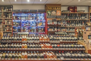 A well-stocked wine and spirits store with numerous bottles of wine displayed on wooden shelves. The shelves feature a range of wines from different regions and spirits in glass bottles, illuminated by soft lighting. Signs indicate different categories such as liqueurs, wines, and special beers.