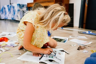 a little girl sitting on the floor looking at a book