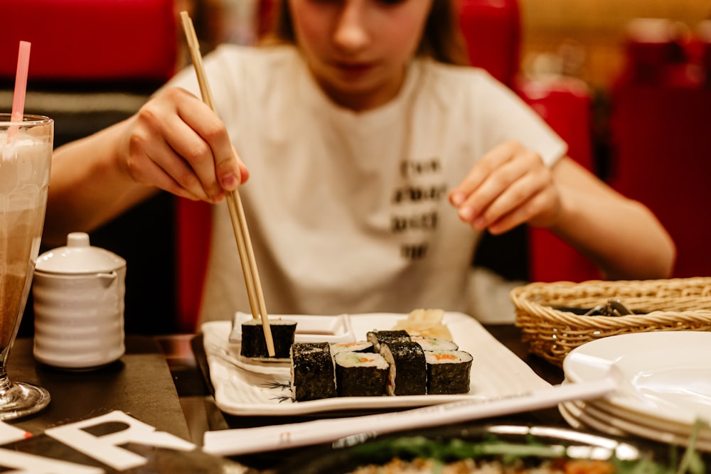 a woman sitting at a table with a plate of sushi and chopsticks