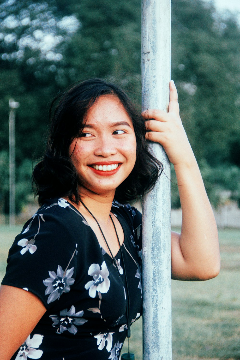 a woman leaning against a pole in a park