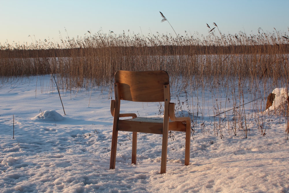 a wooden chair sitting in the middle of a snow covered field