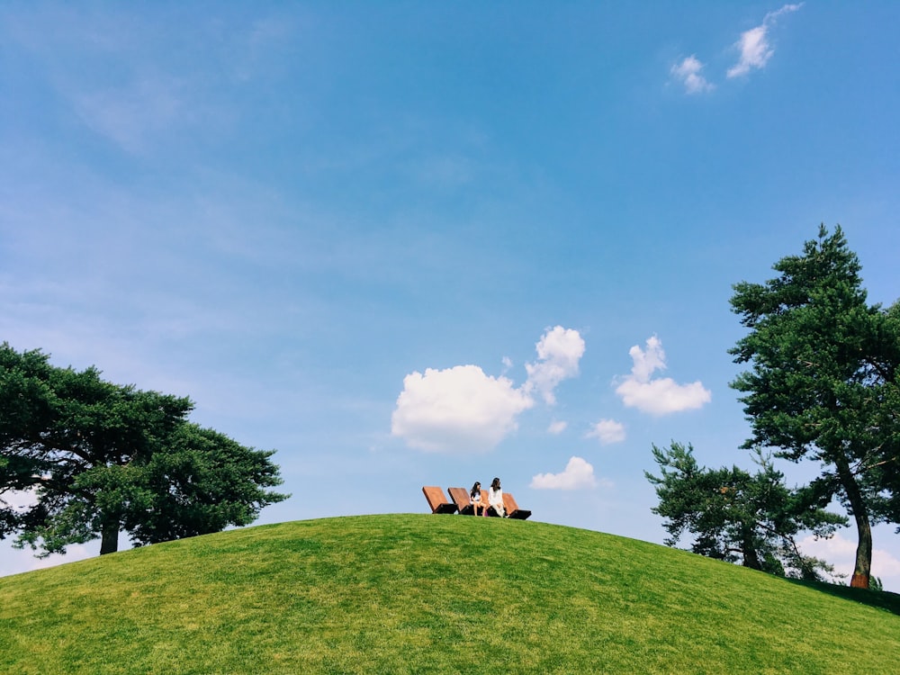a couple of people sitting on top of a green hill