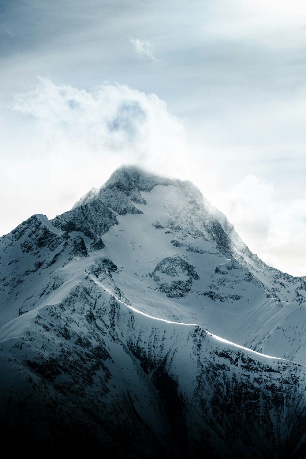 a mountain covered in snow under a cloudy sky