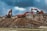 Two large excavators engage in construction work on a rocky site, with overcast clouds adding a dramatic backdrop. The machinery, robust in design and red in color, dominates the scene amidst the earthy tones of the rocky terrain.