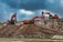 Two large excavators engage in construction work on a rocky site, with overcast clouds adding a dramatic backdrop. The machinery, robust in design and red in color, dominates the scene amidst the earthy tones of the rocky terrain.