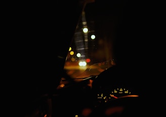 A dimly lit car interior with a focus on the dashboard and the speedometer, showing a speed of around 40 mph. The view through the windshield features bokeh effects from street lights or traffic lights, creating a blurred background with a mix of warm colors.