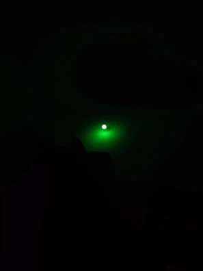 Compact flashlight casting a focused beam with neon green glow highlights.