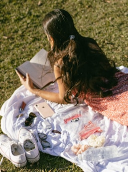 a woman sitting on a blanket reading a book