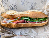 Freshly made savory sandwich with crisp lettuce and juicy tomato, wrapped in parchment paper.
