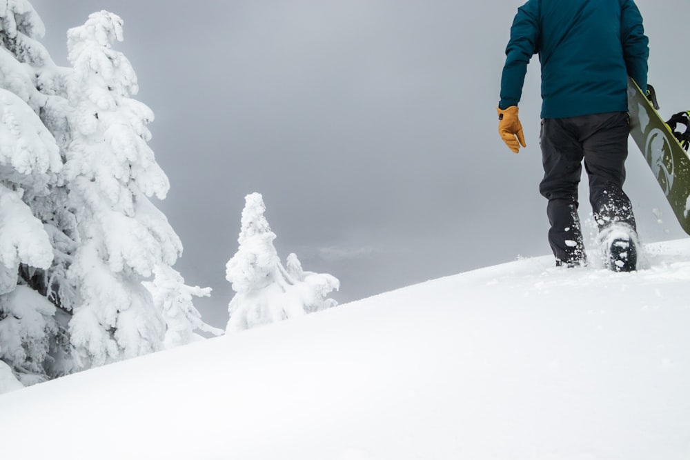 a man walking up a snow covered hill with a snowboard