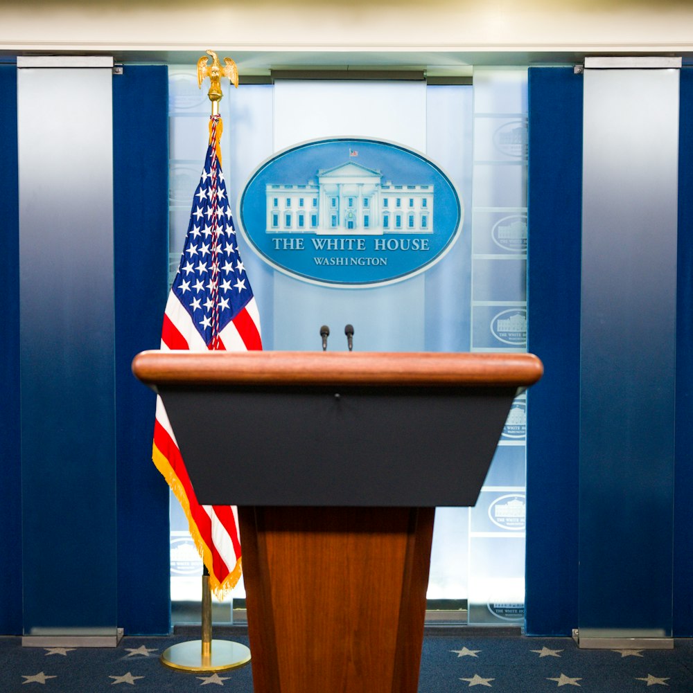 Un podio con una bandera estadounidense y la Casa Blanca