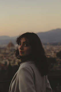 Evening outdoor scene with models posing in elegant coats against a city skyline at dusk.