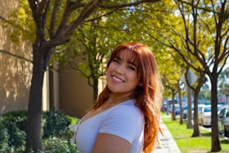 Close-up of a woman with shiny, vibrant red hair smiling outdoors in natural light