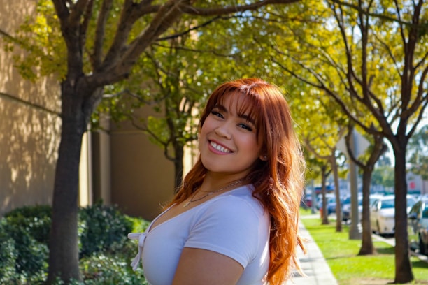 Close-up of a woman with shiny, vibrant red hair smiling outdoors in natural light