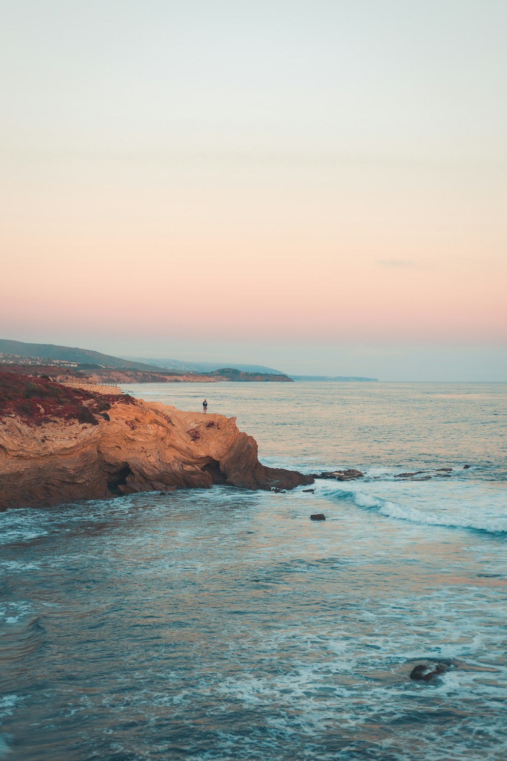 Una persona in piedi sul bordo di una scogliera vicino all'oceano