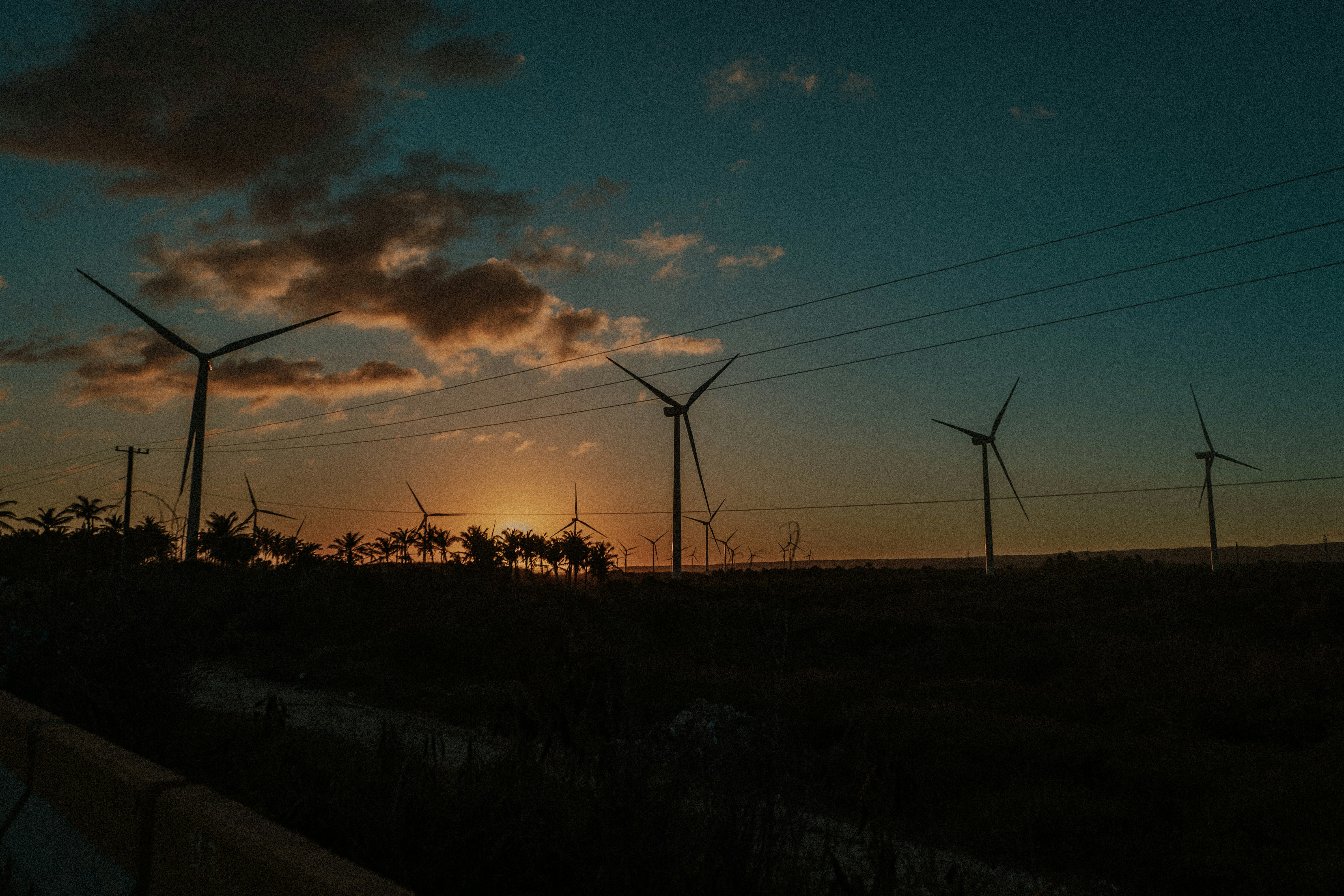 the sun is setting behind a row of windmills