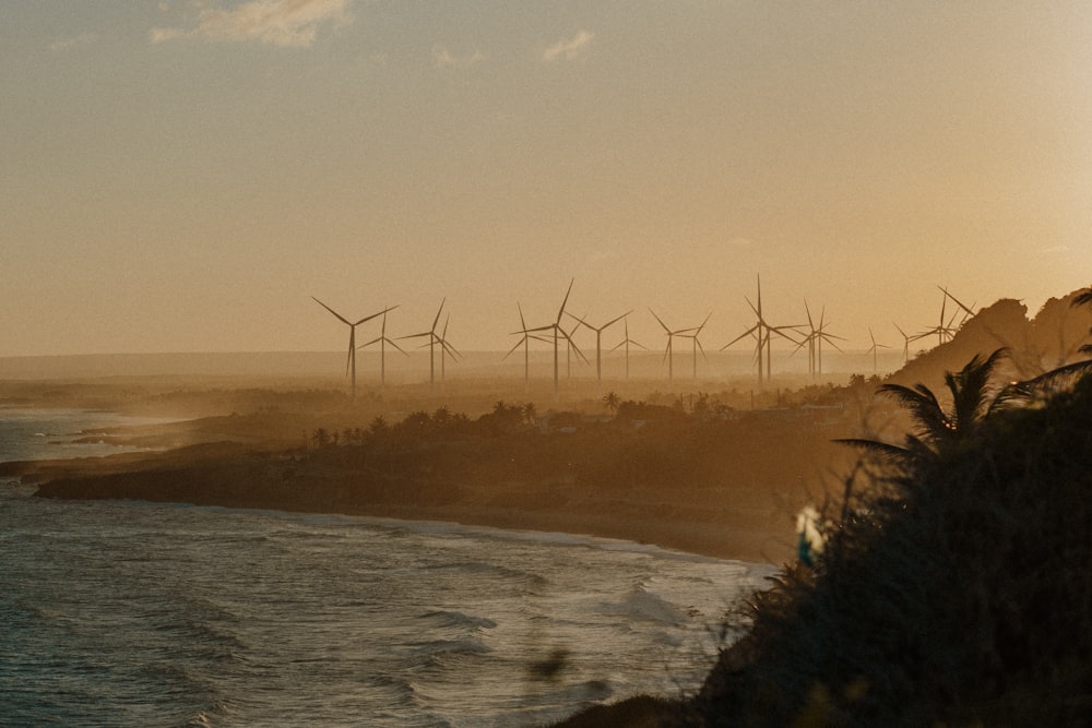 a group of windmills on a hill next to the ocean