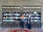 Two individuals are standing in front of two bookcases labeled 'Free Islamic Books.' The bookcases are filled with various books and pamphlets. The man is holding a book, and there is a carpet on the floor.