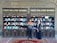 Two individuals are standing in front of two bookcases labeled 'Free Islamic Books.' The bookcases are filled with various books and pamphlets. The man is holding a book, and there is a carpet on the floor.