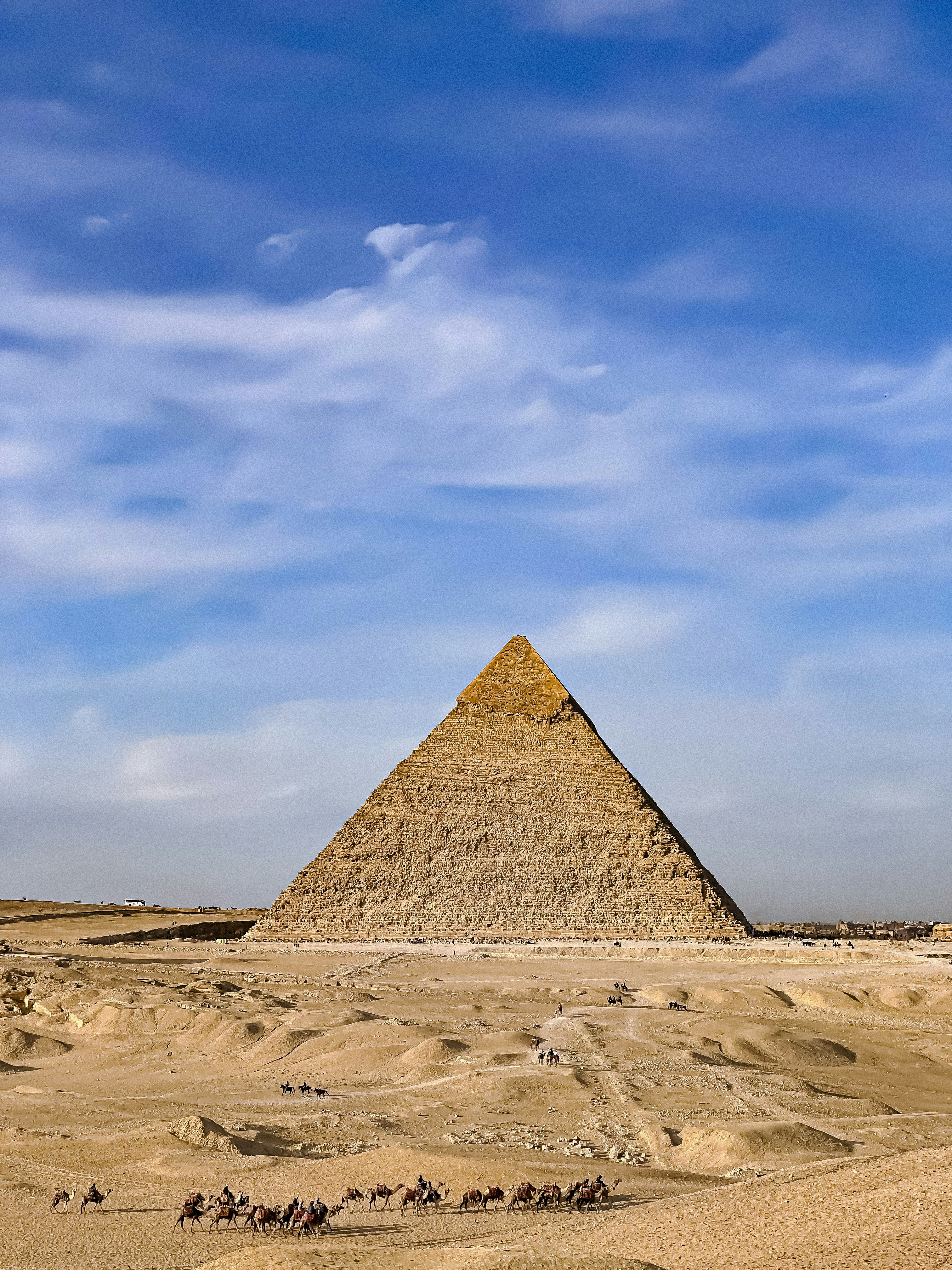 Un grupo de personas montando camellos frente a una pirámide