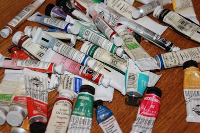 Various vibrant paint tubes and palettes arranged on a wooden table.