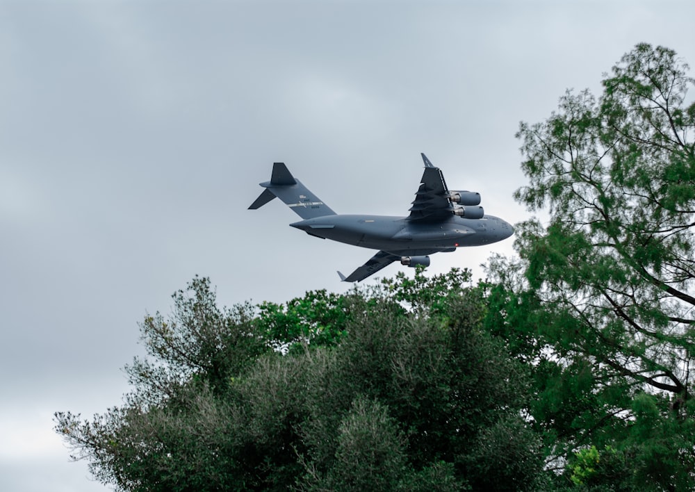 a large airplane flying over a forest filled with trees