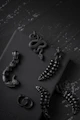 A dark, moody grid of gothic jewelry pieces with subtle silver highlights and crimson accents.