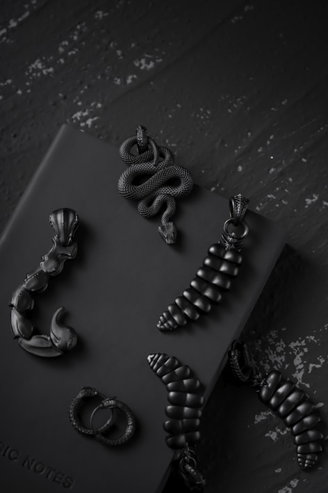 A dark, moody display of handcrafted gothic jewelry with intricate silver details and shadowy gemstones.