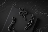 A collection of intricately designed black pendants rests on a dark surface, featuring elements like a coiled snake and segmented shapes reminiscent of marine life or plants.